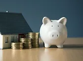 a piggybank gold coins and a miniature house on a table