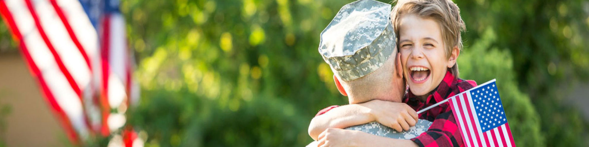 young boy proudly holds an American flag while hugging a soldier