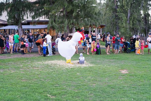 a group of people in a park and a person in chicken garment