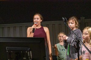 a person singing into a microphone with a child standing behind her<br />
