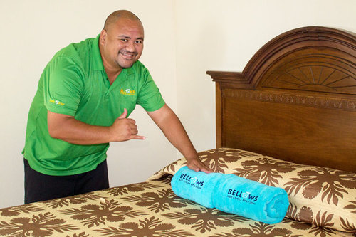 a person in green shirt holding a blue rolled up blanket on a bed<br />
